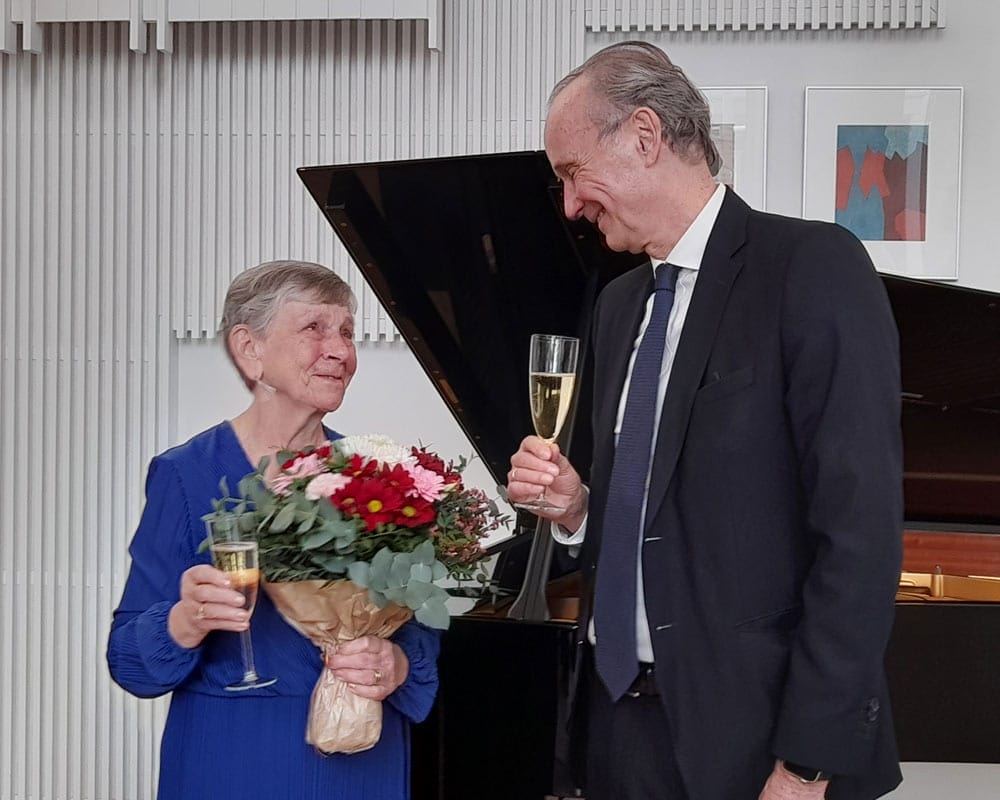 Eine Frau mit Blumenstrauß und ein Mann in Anzug stoßen mit Sekt an