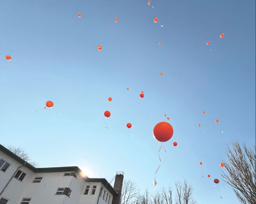 rote Ballons fliegen über ein Haus in den blauen Himmel
