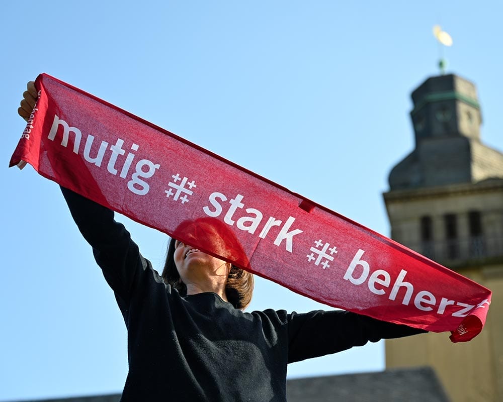 Frau hält roten Schal in die Luft. Im Hintergrund steht eine Kirche