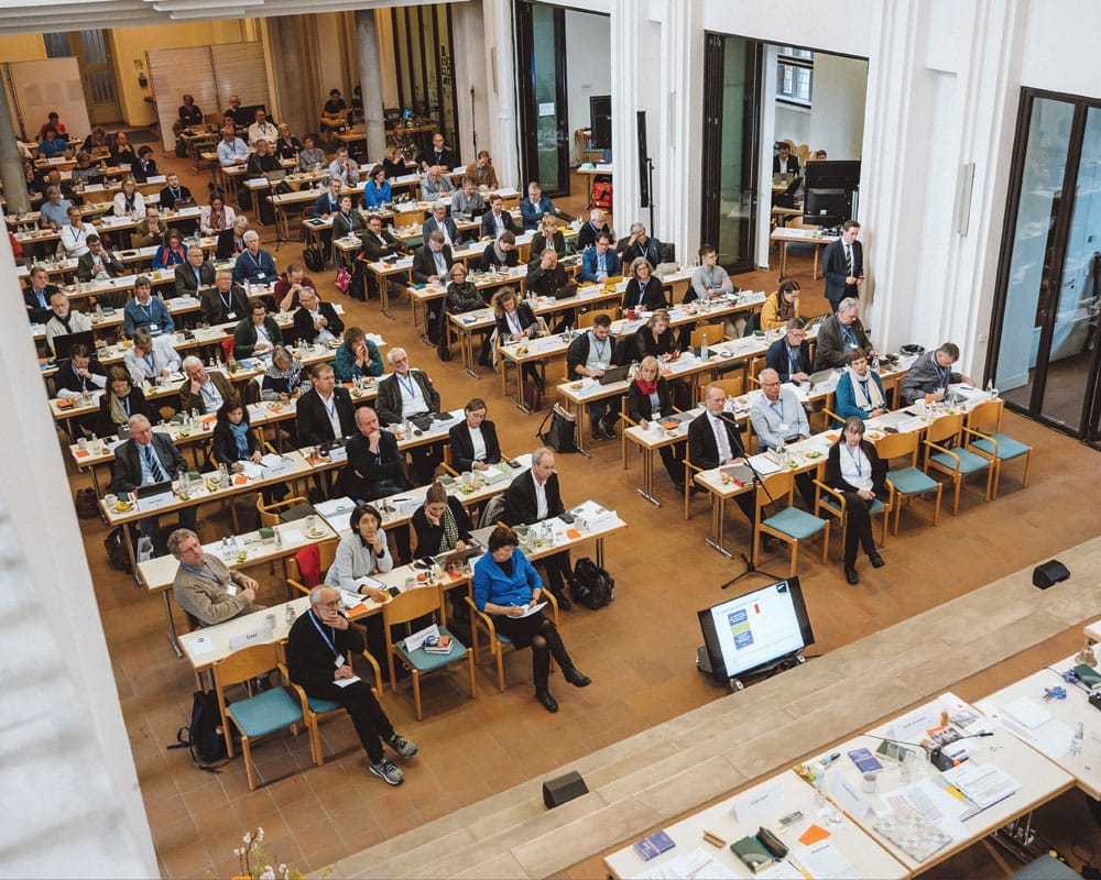 Von oben in einen großen Raum fotografiert, in dem Menschen an Tischen sitzen
