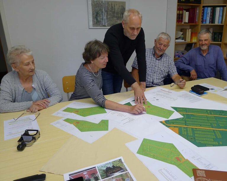 5 Menschen stehen an einem Tisch mit Plänen und Papier