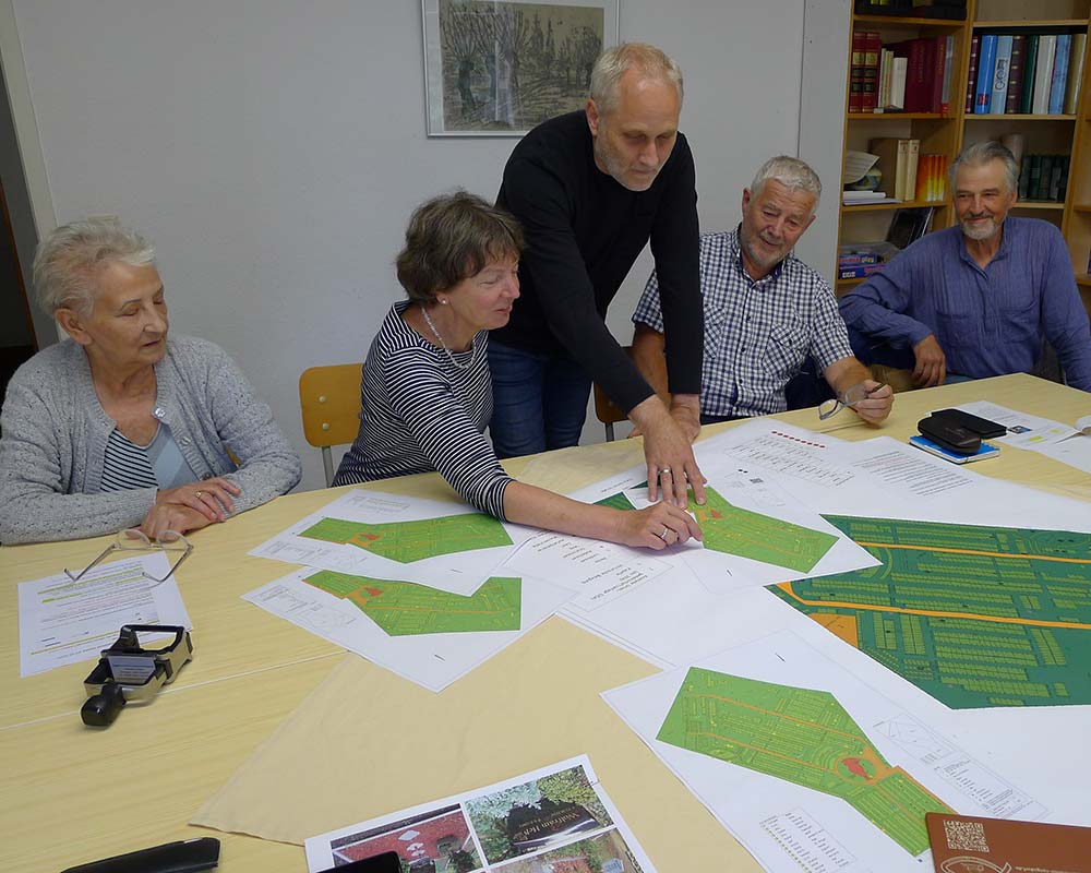 5 Menschen stehen an einem Tisch mit Plänen und Papier