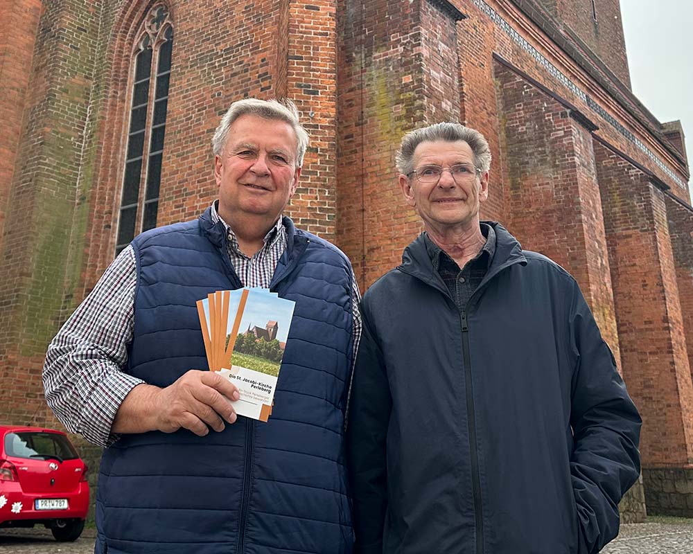 Zwei Männer mit Prospekten stehen vor einer Kirche