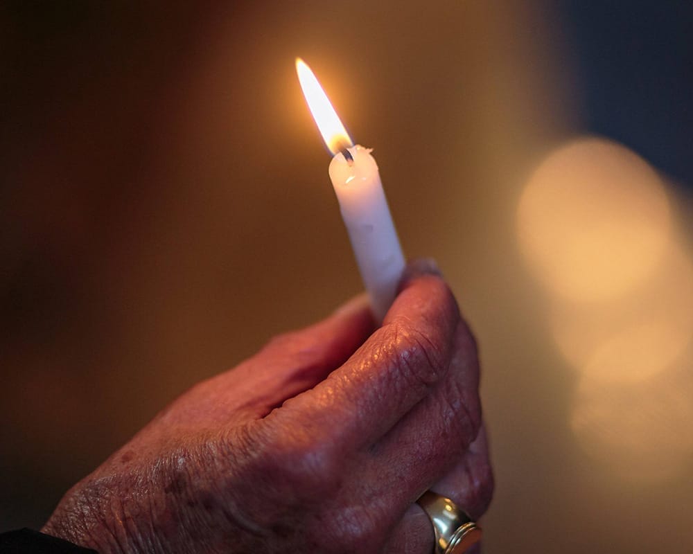Eine Hand hält eine weiße brennende Gedenkkerze