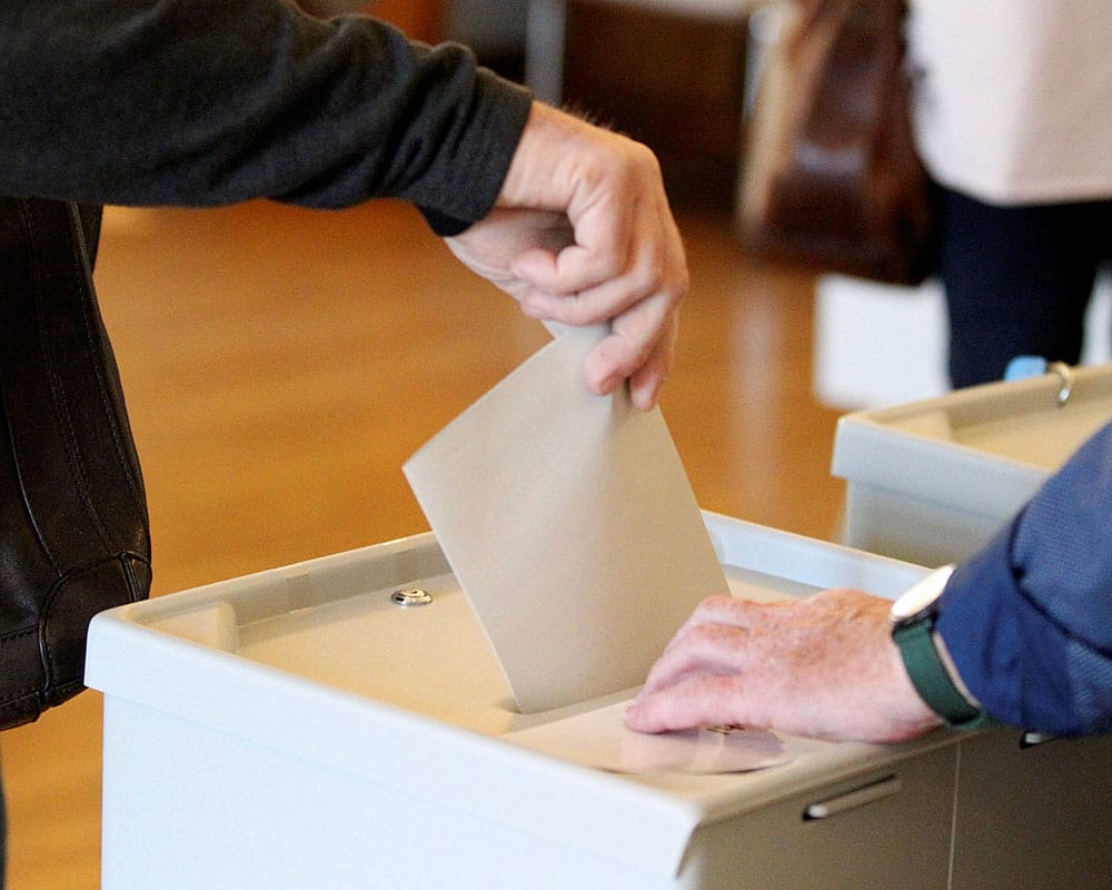 Hand steckt Zettel in Wahlurne